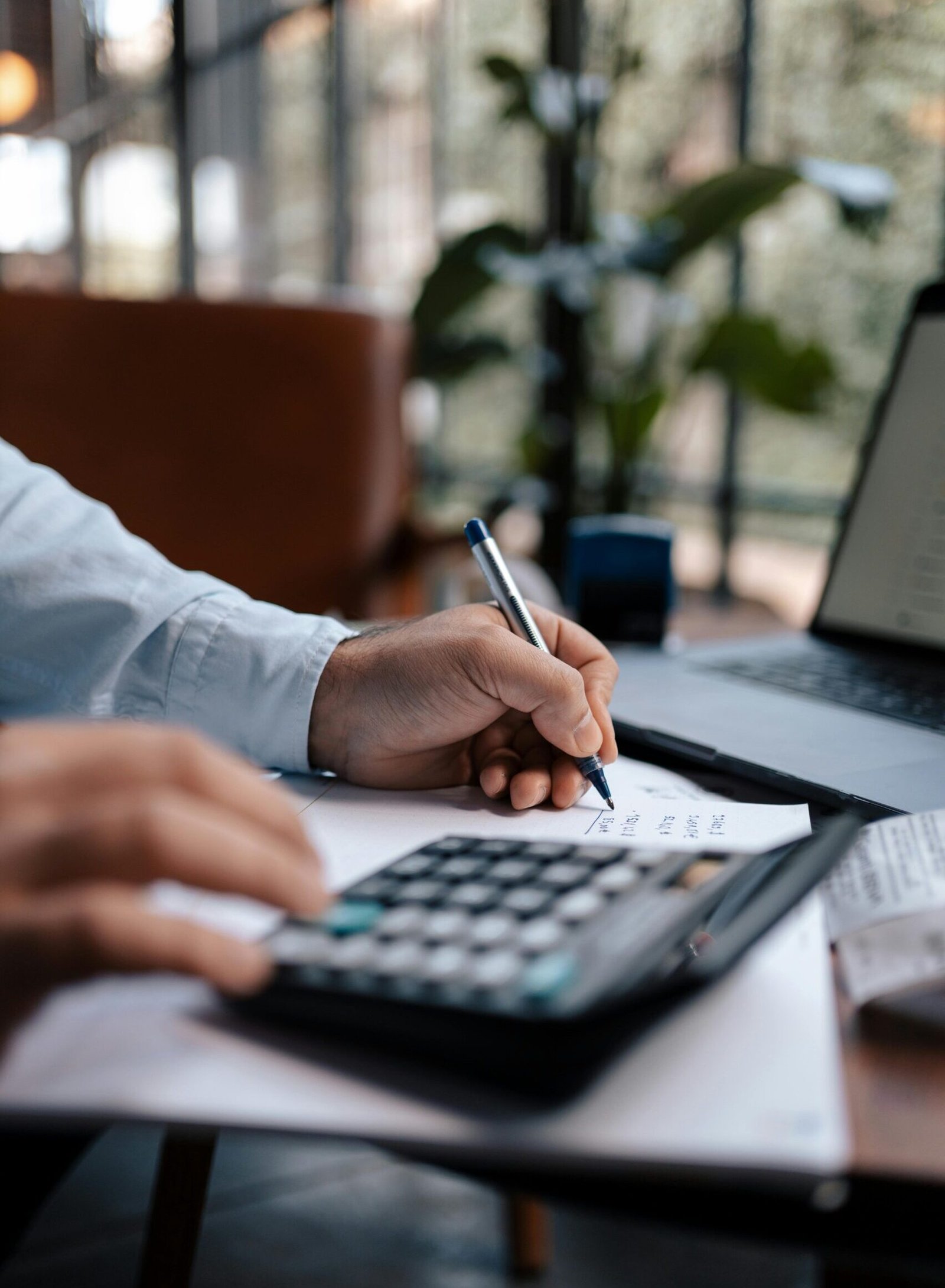 A person calculating finances with a calculator and pen on a desk indoors.